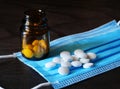 White round pills on disposable medical mask with a brown bottle on dark background