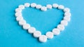 White round pills laid out in the shape of a heart on a blue background. Health symbol made of pills for therapy, treatment and Royalty Free Stock Photo