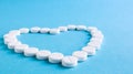 White round pills laid out in the shape of a heart on a blue background. Health symbol made of pills for therapy, treatment and Royalty Free Stock Photo