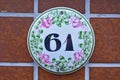 A white, round shaped house number plaque on tile, showing the number sixty one Royalty Free Stock Photo