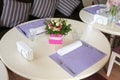 White round table with flower decor, purple napkins and dining appliances. Rose bouquet in elegance cafe interior. Event