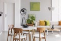 White round table with wooden chairs in the middle of stylish living room with industrial lamp, comfortable couch and golden lime