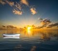 White rowing boat adrift on open ocean and drifting towards the sunset