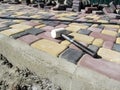 A white rubber hammer lies on the surface of a newly laid paving slab against the background of piles of tiles