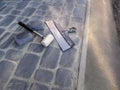 White rubber mallet and a large construction spatula lie on the surface of a newly laid gray paving slab with a concrete edge.