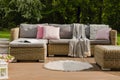 Rug on wooden terrace in stylish garden with wicker furniture with pillows
