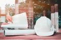 White safety helmet and paper plan blueprint on wood table in working construction site housing building and Double exposure