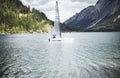 A white sailboat on the body of water surrounded by mountains and hills covered with trees