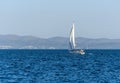 White sailboat glides through a vast ocean with a picturesque shoreline in the background.