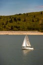 White sailboat sailing across a tranquil lake on a sunny day