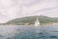 White sailboat sails on the sea along the mountainous coast