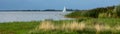White sailboat on the water in a bay between reed banks under a dark blue sky, leisure activity in the nature, panoramic format,
