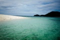 White sand beach on lonely island in tropical sea, light blue green sea, blue sky with white clouds