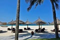 On the white sand of the beach, there are sun umbrellas, sun loungers, and palm trees.