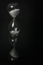 White sand hourglass on a black mirror surface with reflections isolated on black Royalty Free Stock Photo
