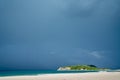 White sandy beach and Leisure Island caught in sun against background dark blue raincloud sky