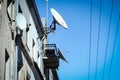 White satellite dish antennas on the roof and wall of ann old building with lines or wires on blue sky background Royalty Free Stock Photo