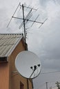 A white satellite dish and an iron television antenna on a brown wall of a house Royalty Free Stock Photo