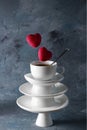 White saucer pyramid cup of tea with spoon on top. With two candy red hearts flying over Dark background. Creative concept,