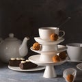 White saucer pyramid with cup of tea on top decorated with chocolate truffles on surved dessert table on dark background. Creative