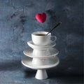 White saucer pyramid with cup of tea on top and flying red hearts candy over it. Dark background. Creative concept, love,