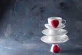 White saucer pyramid with cup of tea on top and two red hearts candy on it Dark background. Creative concept, love, relations,