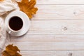 White scarf, cup of coffee and dry yellow leaves on a wooden table. Autumn mood, copy space