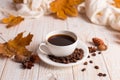 White scarf, a cup of coffee with scattered coffee beans, dry yellow leaves on a wooden table. Autumn mood, copy space Royalty Free Stock Photo