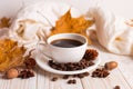 White scarf, a cup of coffee with scattered coffee beans, dry yellow leaves on a wooden table. Autumn mood, copy space Royalty Free Stock Photo