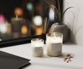 White scented candle in glass with blank label mockup with aroma reed diffuser and vase with blured night city lights background,