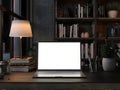 A white-screen laptop computer mockup and books on a table in a modern dark room Royalty Free Stock Photo