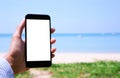 A white screen mobile smartphone on a woman`s hand in front the white sand beach blue sea and sky Royalty Free Stock Photo