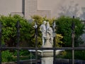 White sculpture with a male and female on an empty fountain behind the metal fence