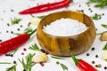 White sea salt in a round wooden bowl with red chilli pepper, peppercorns, garlic and rosemary on food background. Royalty Free Stock Photo