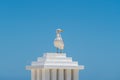 A white seagull is sitting, standing on a stepped white pole with a roof against the background of a clear blue sky Royalty Free Stock Photo