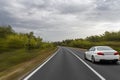 A white sedan speeds down a curved, tree-lined highway under a cloudy sky Royalty Free Stock Photo