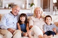 White senior couple and their grandchildren sitting on a sofa together at home smiling to camera Royalty Free Stock Photo