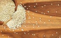 White sesame seeds pouring from small cup to wooden table, view from above Royalty Free Stock Photo
