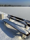 White shades of winter, a snow-covered bench by a frozen pond