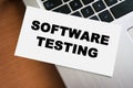 A white sheet of paper displaying the phrase SOFTWARE TESTING in bold letters is placed on a wooden table next to a silv Royalty Free Stock Photo