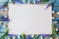 A white sheet of paper framed with purple flowers and quail eggs on a worn blue wooden table. Flat lay with copy space Royalty Free Stock Photo