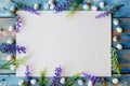 A white sheet of paper framed with purple flowers and quail eggs on a worn blue wooden table. Flat lay with copy space Royalty Free Stock Photo