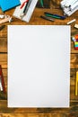 A white sheet of paper sits on a wooden table with a variety of writing utensils