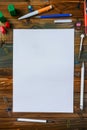 A white sheet of paper sits on a wooden table with a variety of writing utensils