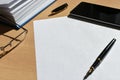 White sheet of paper on a wooden desktop in the office, pen, smartphone, accessories, glasses, copy space