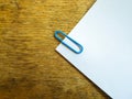 White sheet of paper on a wooden table with a blue paper clip