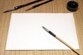 White sheet of washi paper, chinese brushes and inkwell on cane matting background