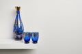 white shelf with a blue glass bottle and two glasses of the same family Royalty Free Stock Photo