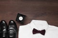 White shirt with stylish burgundy bow tie, wristwatch and shoes on wooden background, flat lay. Space for text