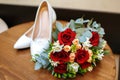 White shoes of the bride with a bouquet of red roses lie on the table in the hotel room Royalty Free Stock Photo